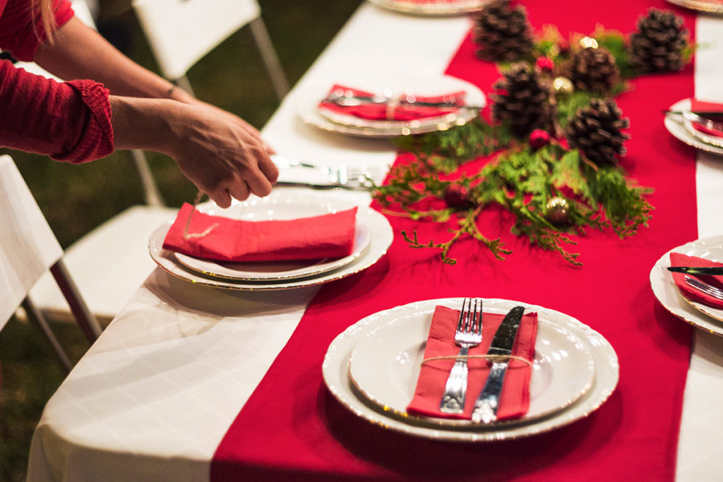Mesa navideña con platos decorados y mano sirviendo comida