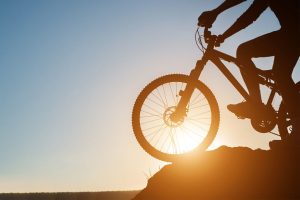 Ciclista montado bicicleta con el sol al fondo, enfocado en la rueda