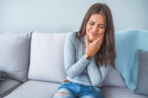 Mujer con expresión de dolor tacándose la mandíbula, sentada en un sofá